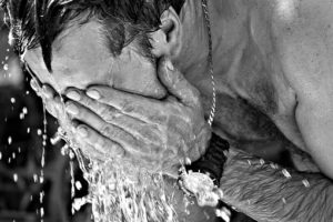猛暑の中顔に水を浴びる男性